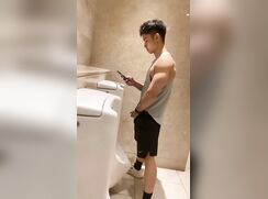 A handsome young boy is pissing in the toilet.